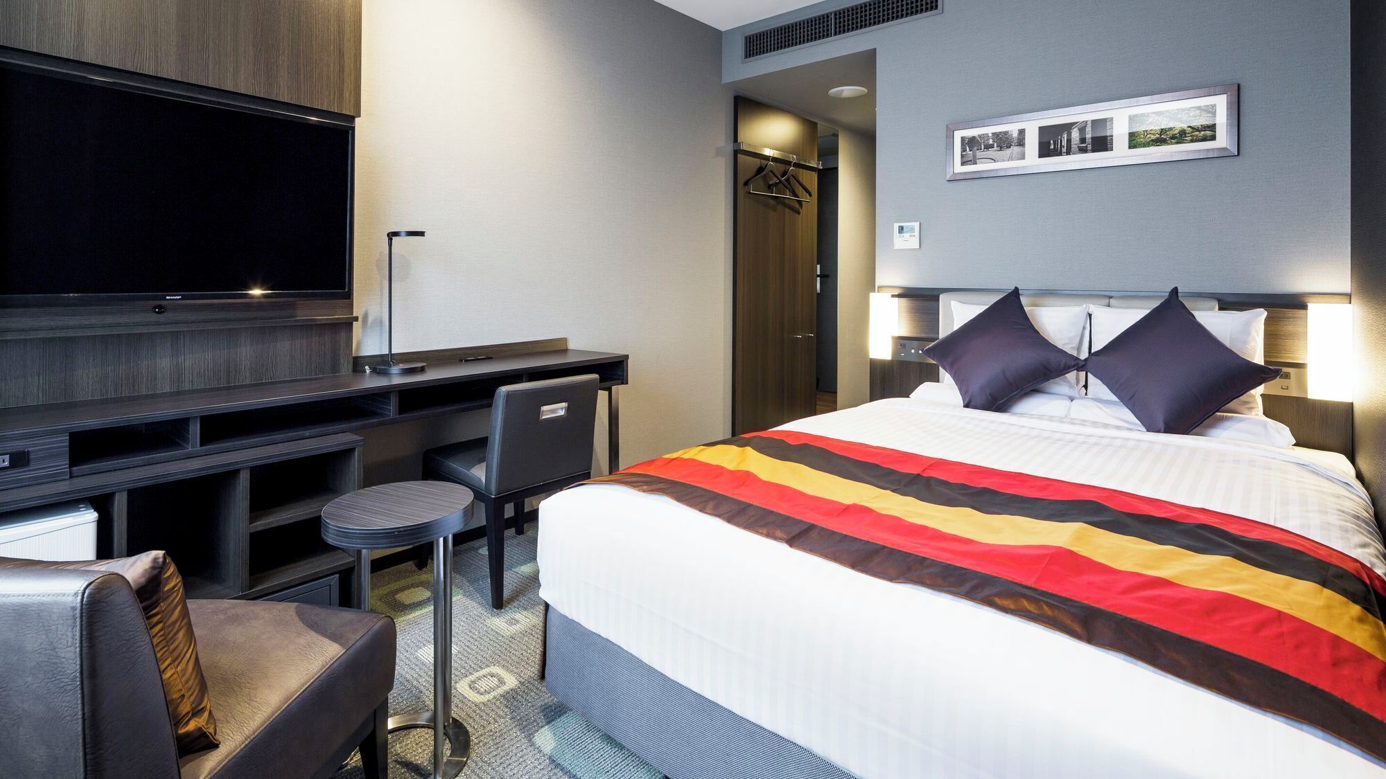Una habitación de hotel con cama, escritorio, silla, televisor y armario.