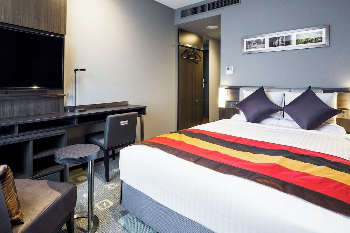 Una habitación de hotel con cama, escritorio, silla, televisor y armario.