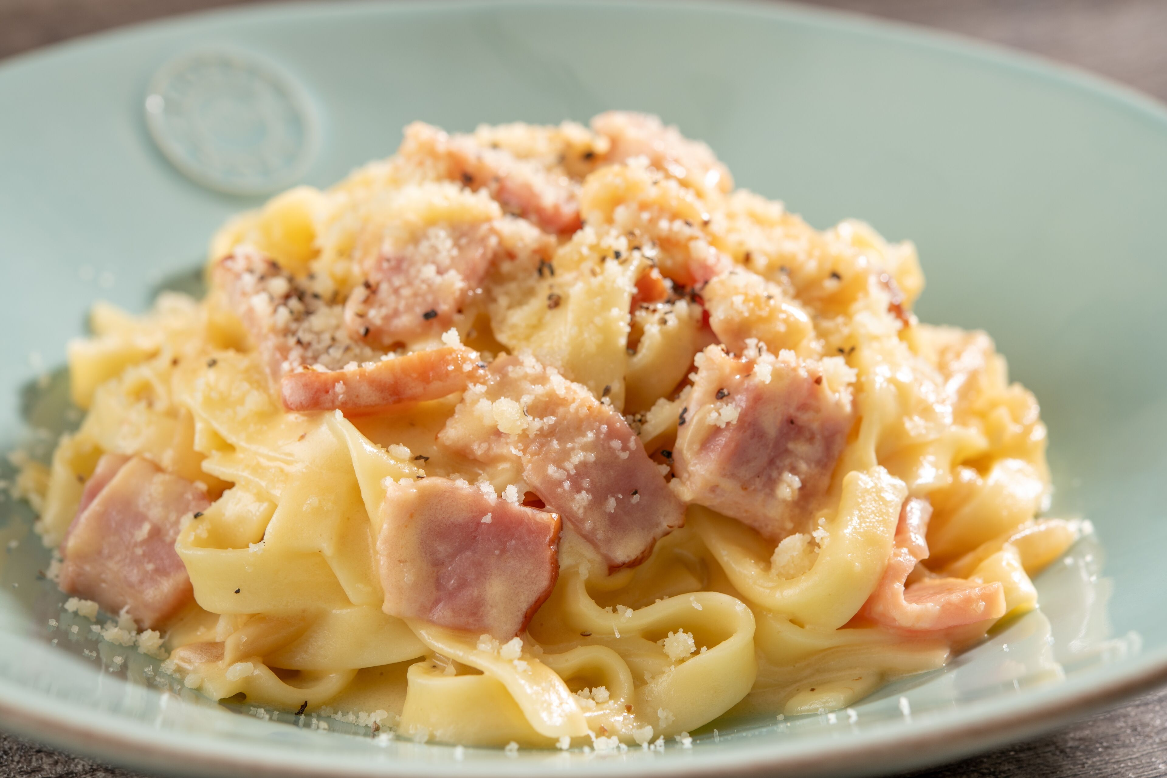 A plate of pasta with ham and grated cheese.