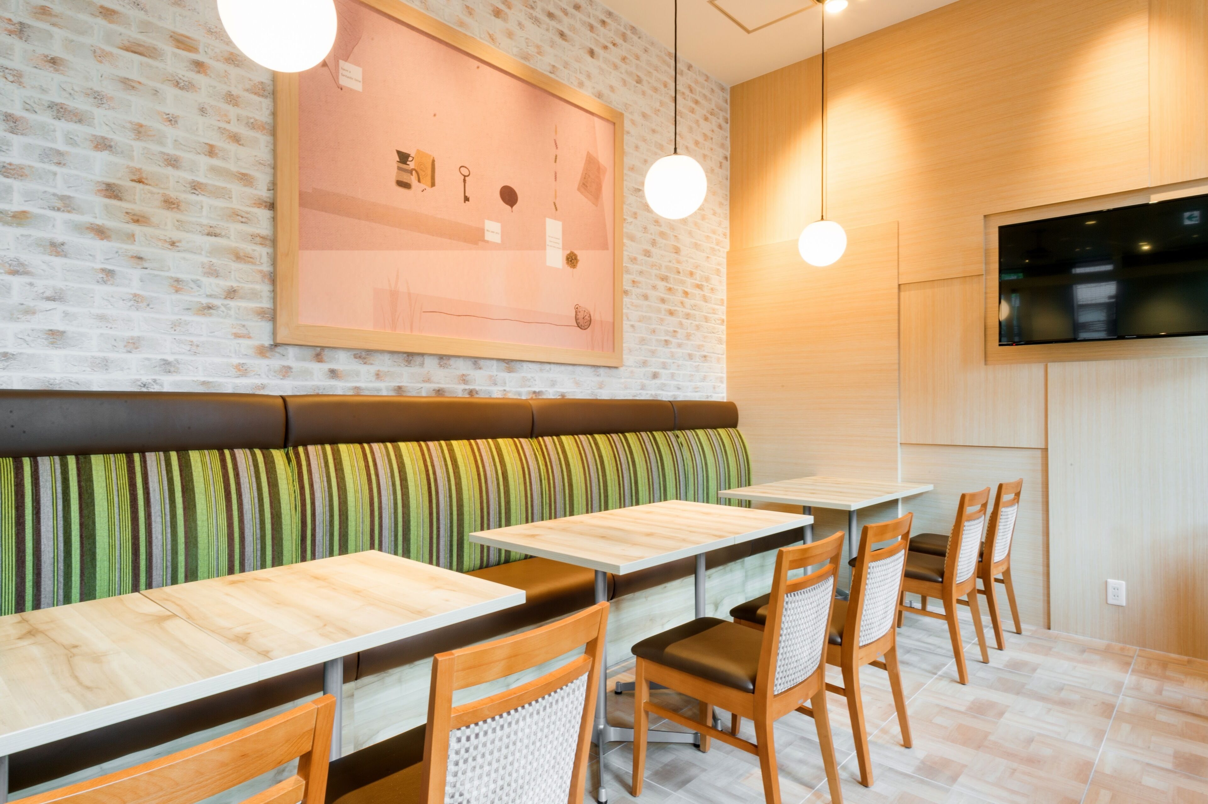 Un restaurante con mesas y sillas de madera, una pared de ladrillo con un cuadro enmarcado e iluminación colgante.