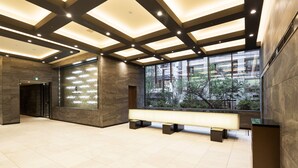 A spacious lobby with a high ceiling, recessed lighting, a large bench, and a view of the outdoors through large windows. - Hotel Mystays Premier Akasaka (Tokyo)