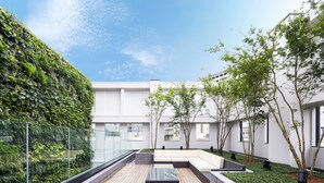 A modern outdoor seating area with a wooden deck, a glass balustrade, and a lush vertical garden. - Hotel Mystays Premier Akasaka (Tokyo)
