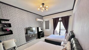 Een moderne hotelkamer met een wand in baksteenmotief, een flatscreen-televisie, een bureau met stoel, een bed met hoofdeinde, en een balkon met een tafel en stoelen.
