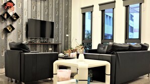 Een moderne woonkamer met een zwarte bank, een witte salontafel en een flatscreen televisie bevestigd aan een muur met behang.