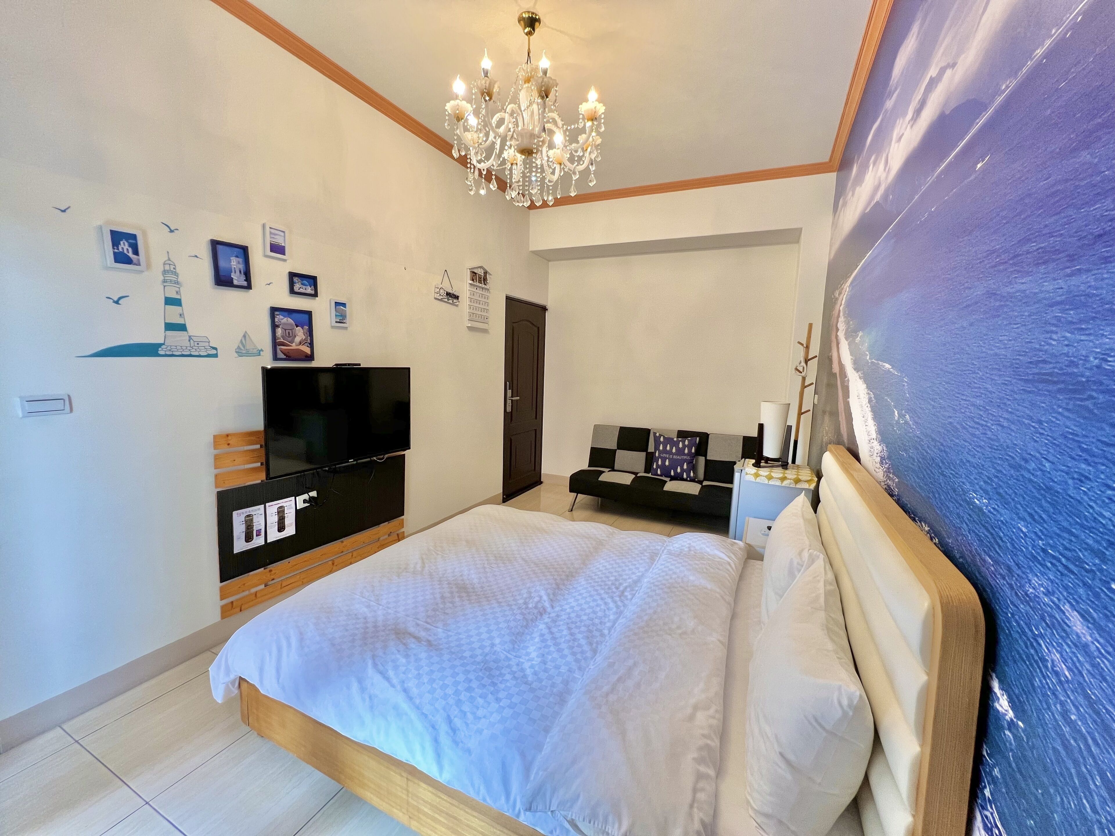A bedroom with a bed, a TV, a chandelier, a painting, and a wall with nautical-themed decorations.