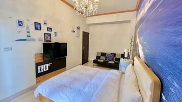 A bedroom with a bed, a TV, a chandelier, a painting, and a wall with nautical-themed decorations.