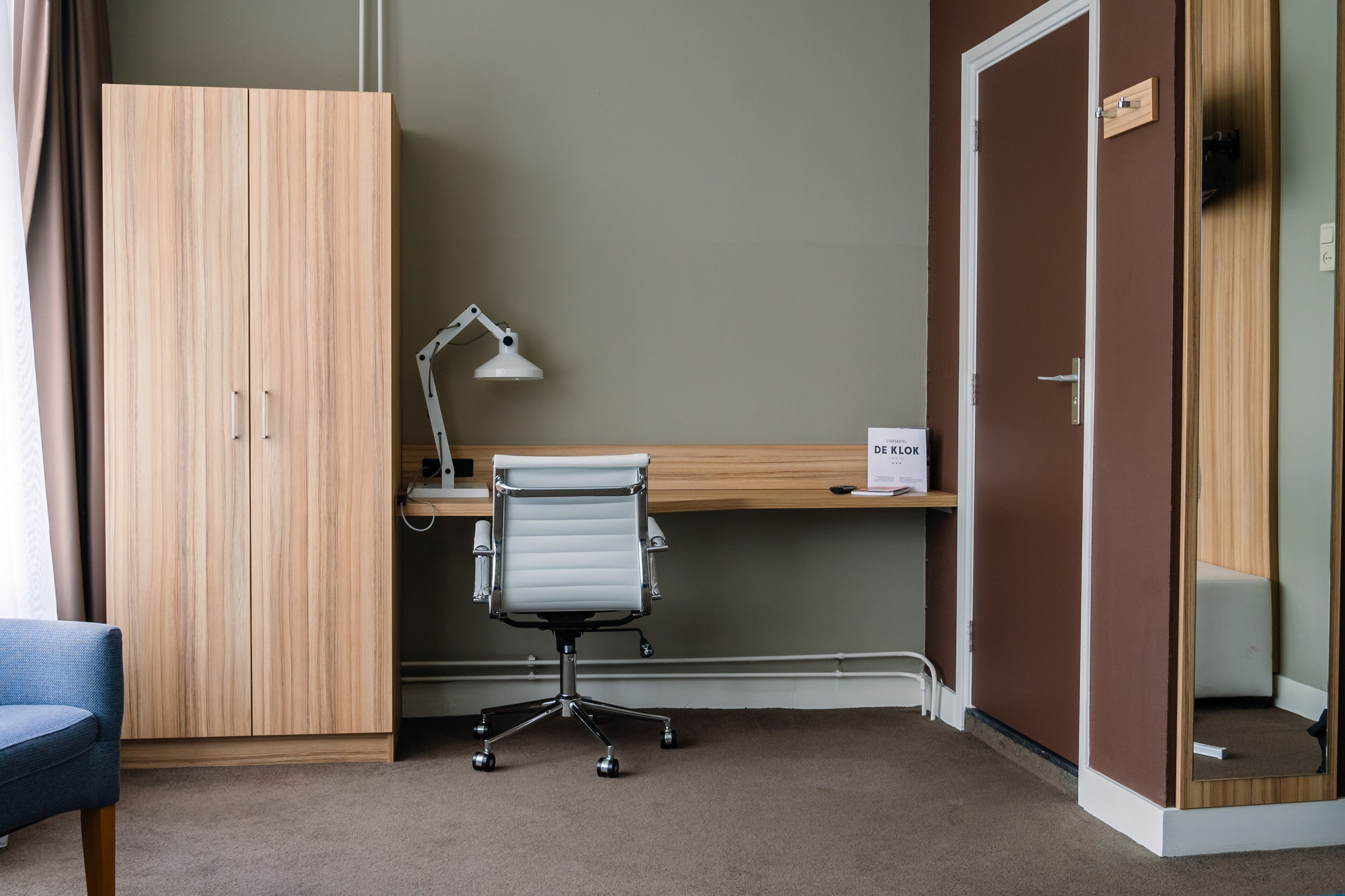 Een hotelkamer met een houten kledingkast, een bureau met stoel, een bureaulamp en een bord aan de muur.