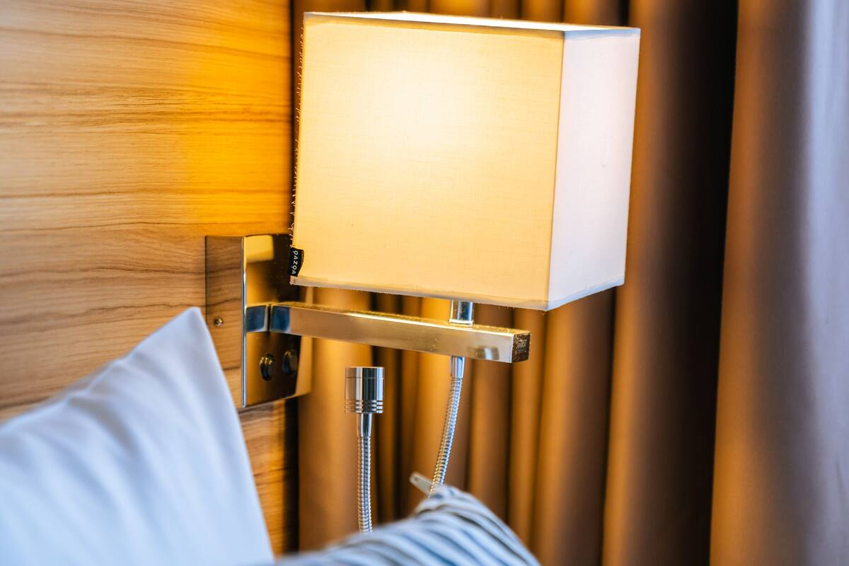 Une chambre d’hôtel avec une tête de lit en bois, une lampe de chevet, un coussin à rayures et un rideau.