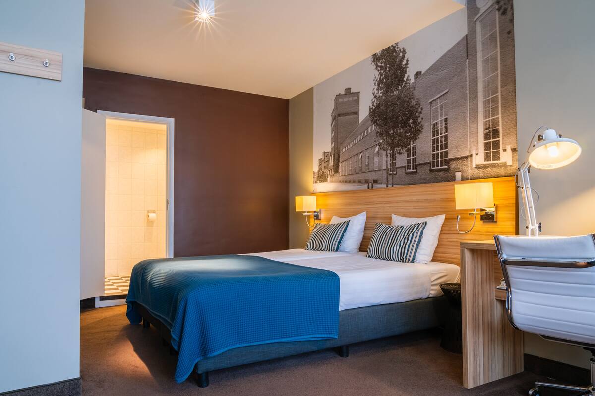 Une chambre d’hôtel équipée d’un lit, d’un bureau, d’une chaise, d’une lampe et d’un tableau accroché au mur.