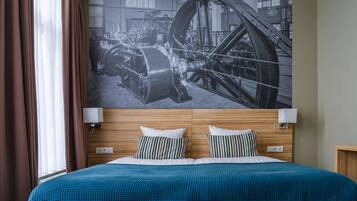 Habitación de hotel con una cama grande, cabecero de madera, dos lámparas de noche y un mural de gran tamaño con temática industrial.