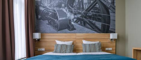A hotel room with a large bed, wooden headboard, two bedside lamps, and a large industrial-themed wall mural.