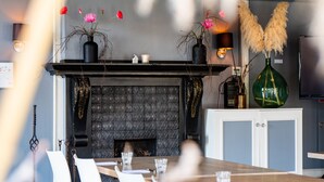 Un coin repas avec une cheminée, des chaises blanches et une longue table en bois.