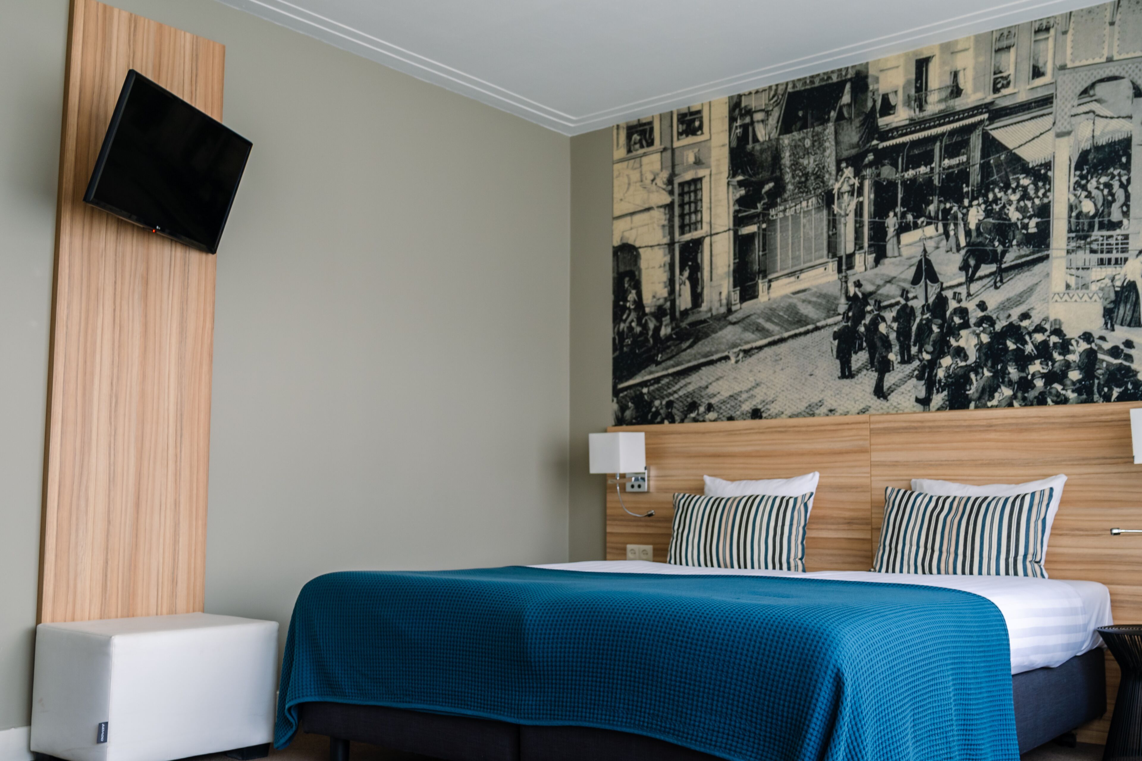 Habitación de hotel con una cama, un televisor montado en la pared y un gran mural en blanco y negro.
