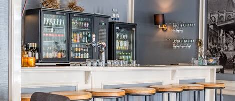 A bar area with wooden stools, a bar counter, and a hanging light fixture.
