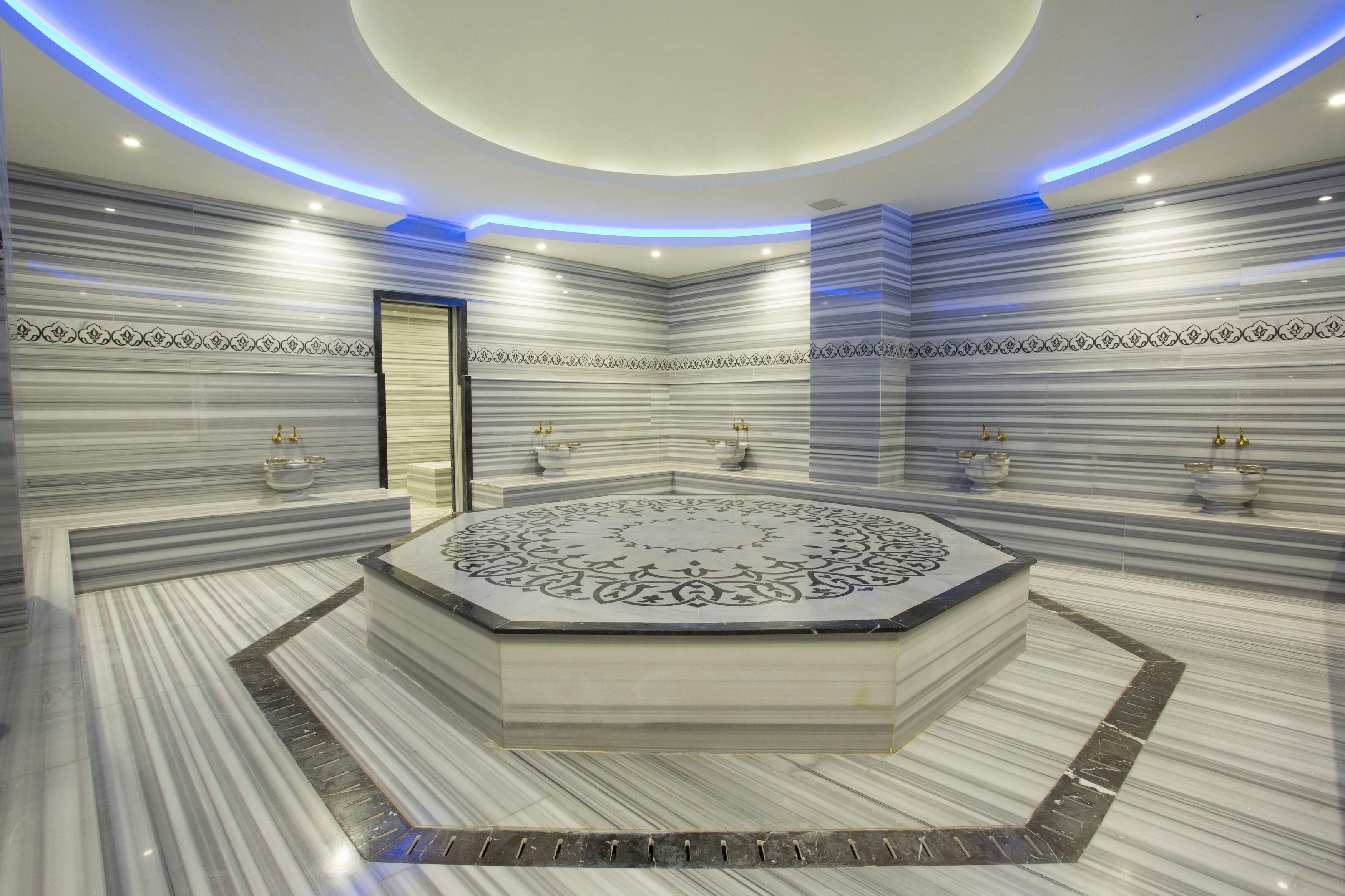A luxurious bathroom with a central circular marble design, marble walls, and gold fixtures.
