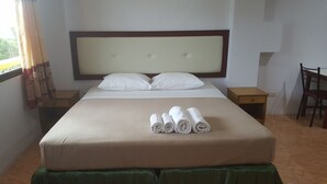 A neatly made bed with a headboard, two pillows, and rolled towels on a green ottoman. - Mood Mansion (Kamala)