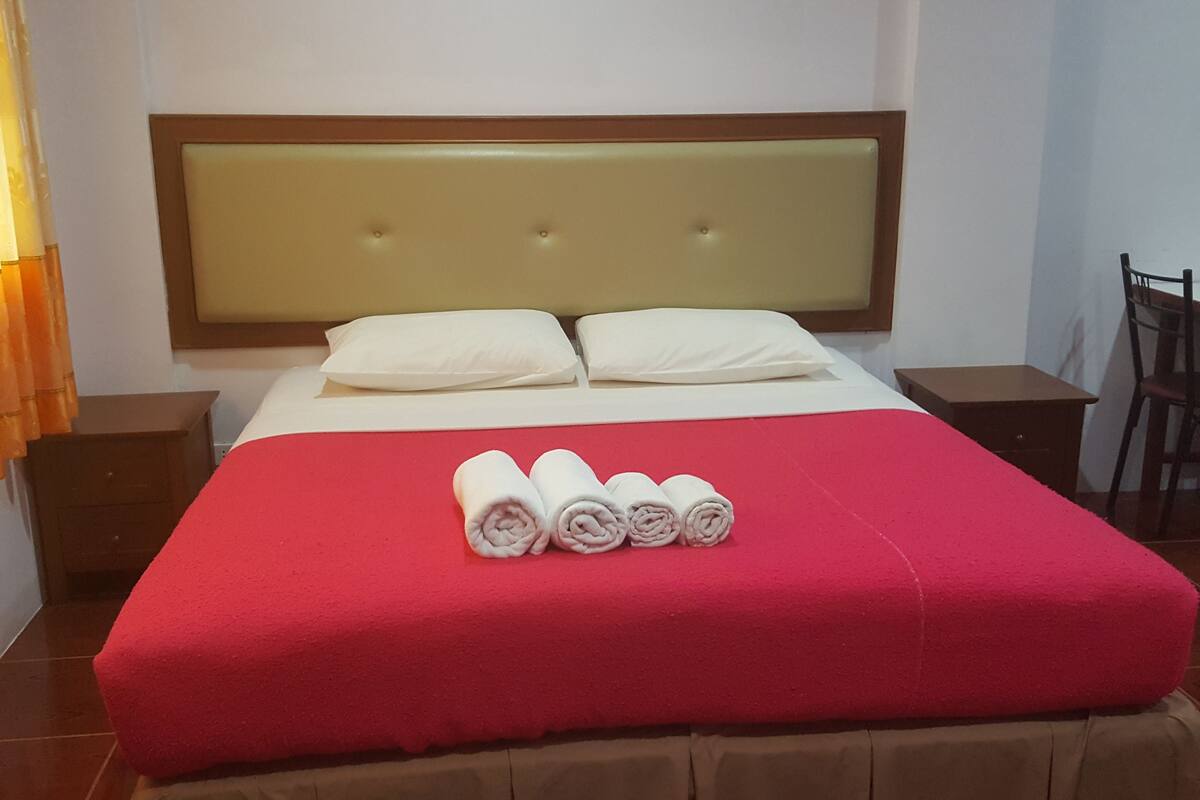 Ein Hotelzimmer mit einem großen Bett, zwei weißen Kissen, einer roten Bettdecke und aufgerollten Handtüchern auf dem Bett.