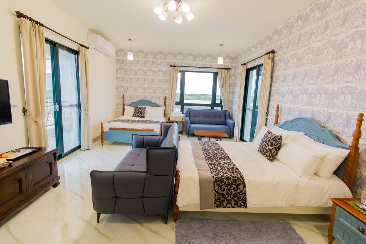 Habitación de hotel con una cama grande, dos sofás, un televisor y vistas al exterior.