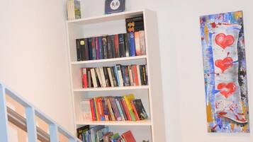 A bookshelf with books and board games, a painting on the wall, and a staircase.