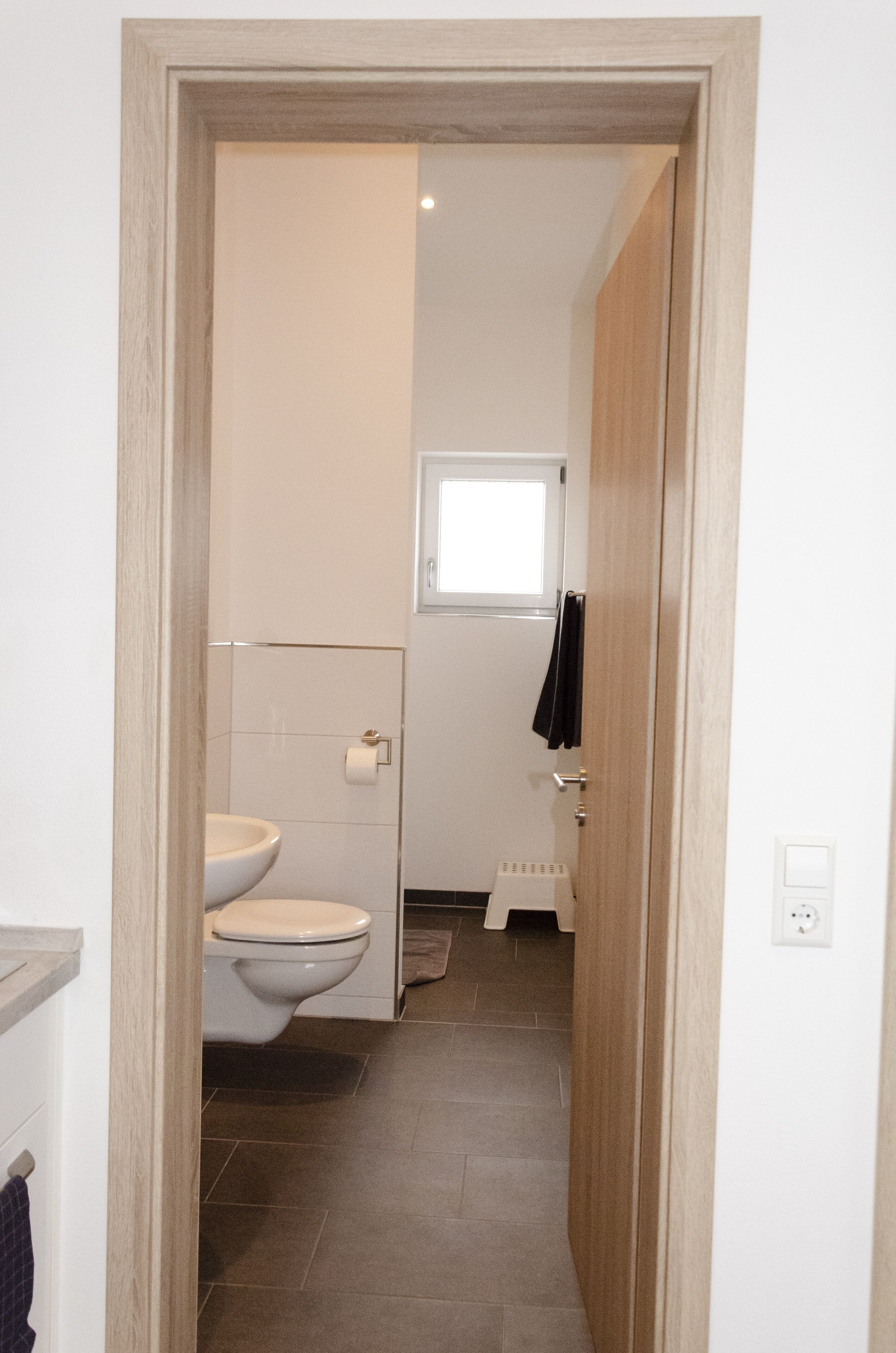 Un pasillo estrecho que conduce a un baño con inodoro, una ventana pequeña y un perchero.