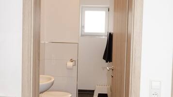 Un pasillo estrecho que conduce a un baño con inodoro, una ventana pequeña y un perchero.