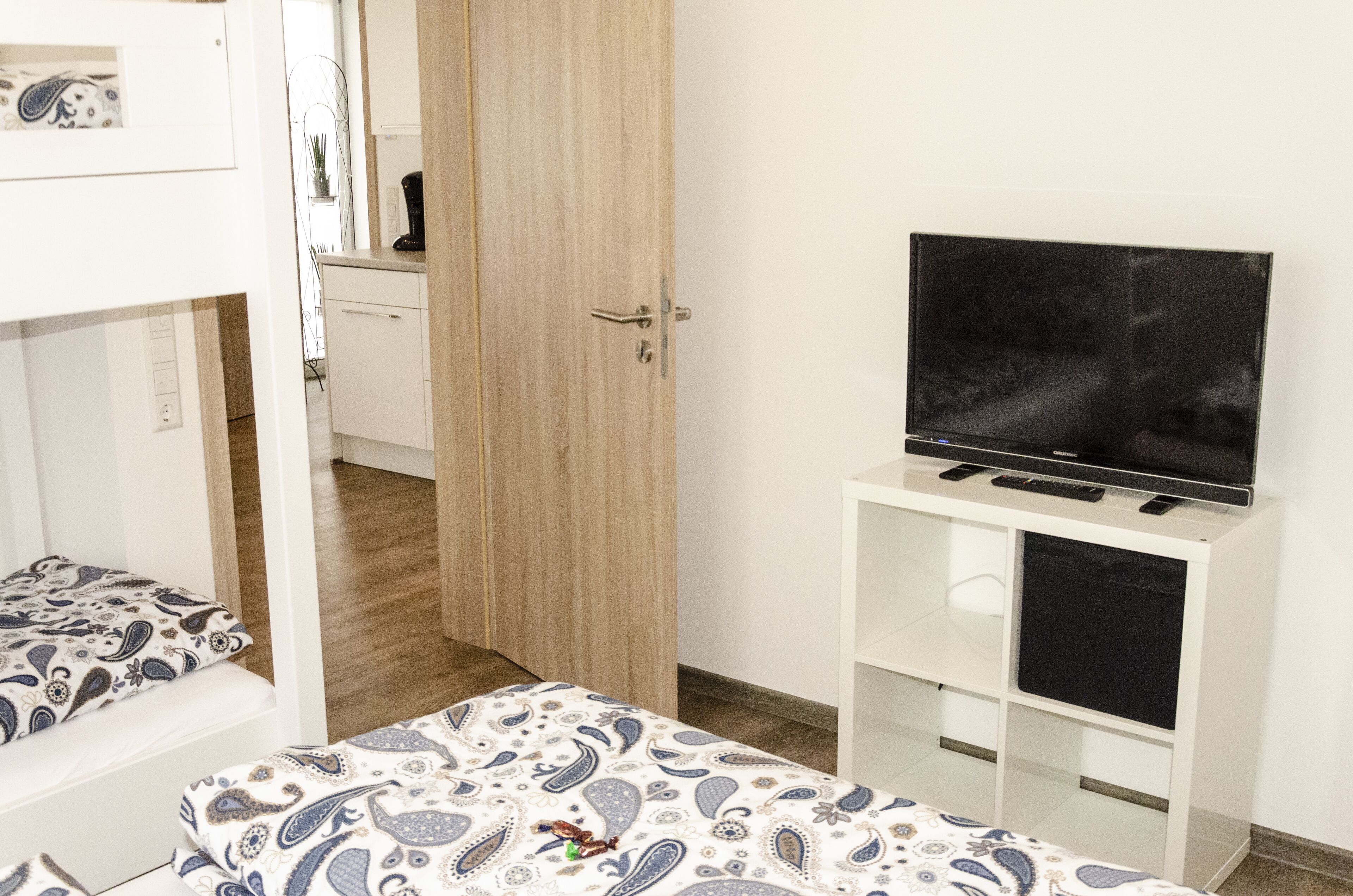 Un dormitorio con una cama, un televisor sobre un mueble y una puerta de madera.