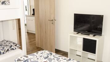 Un dormitorio con una cama, un televisor sobre un mueble y una puerta de madera.