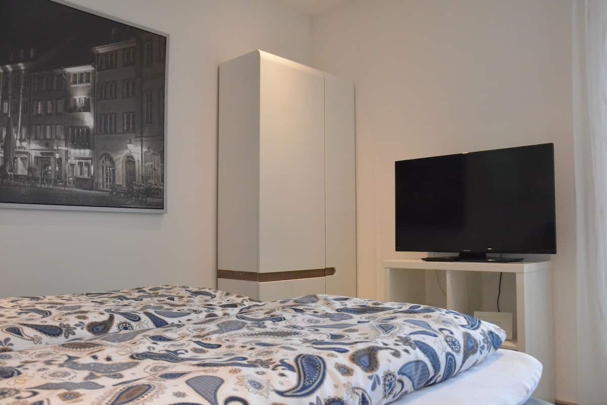 A hotel room with a bed, a wardrobe, a television on a stand, and a framed picture on the wall.