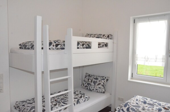 A bunk bed room with patterned bedding and a window with a view of a grassy area.