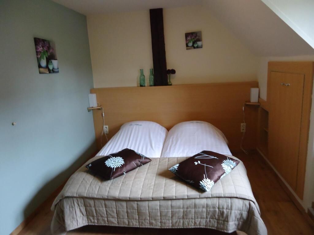 Een slaapkamer met een bed, twee kussens, een nachtkastje, een wandplank en een deur.