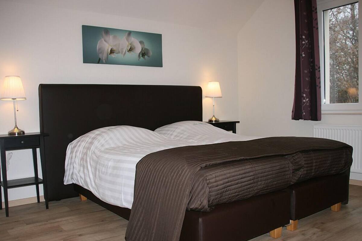 A bedroom with a bed, two bedside tables, a nightstand, a window with curtains, and a wall-mounted picture.