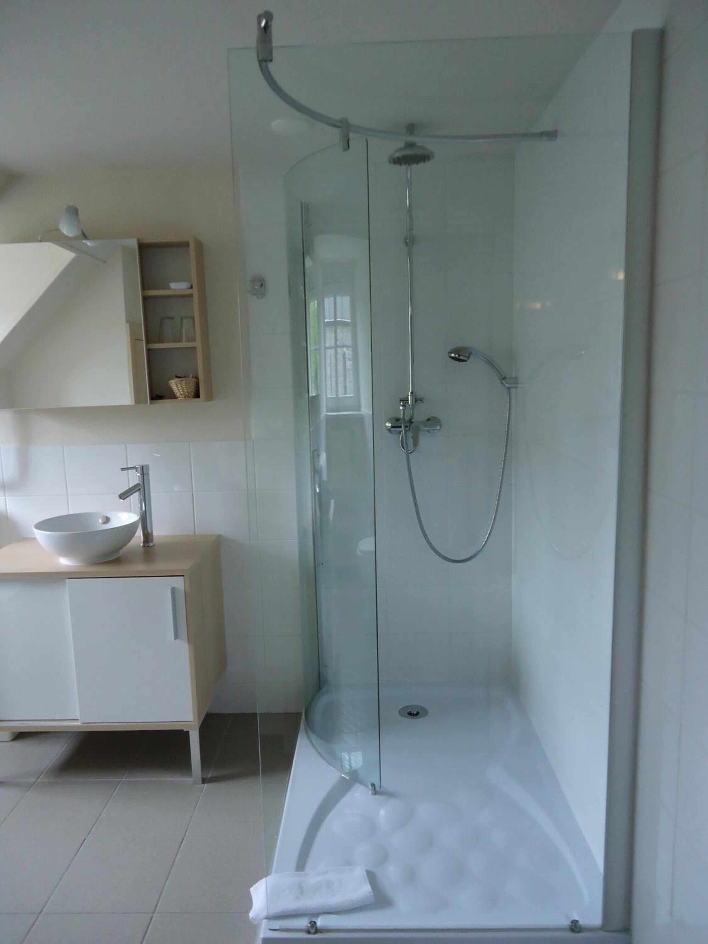 A modern bathroom with a glass-enclosed shower, a white sink, and a wooden vanity.