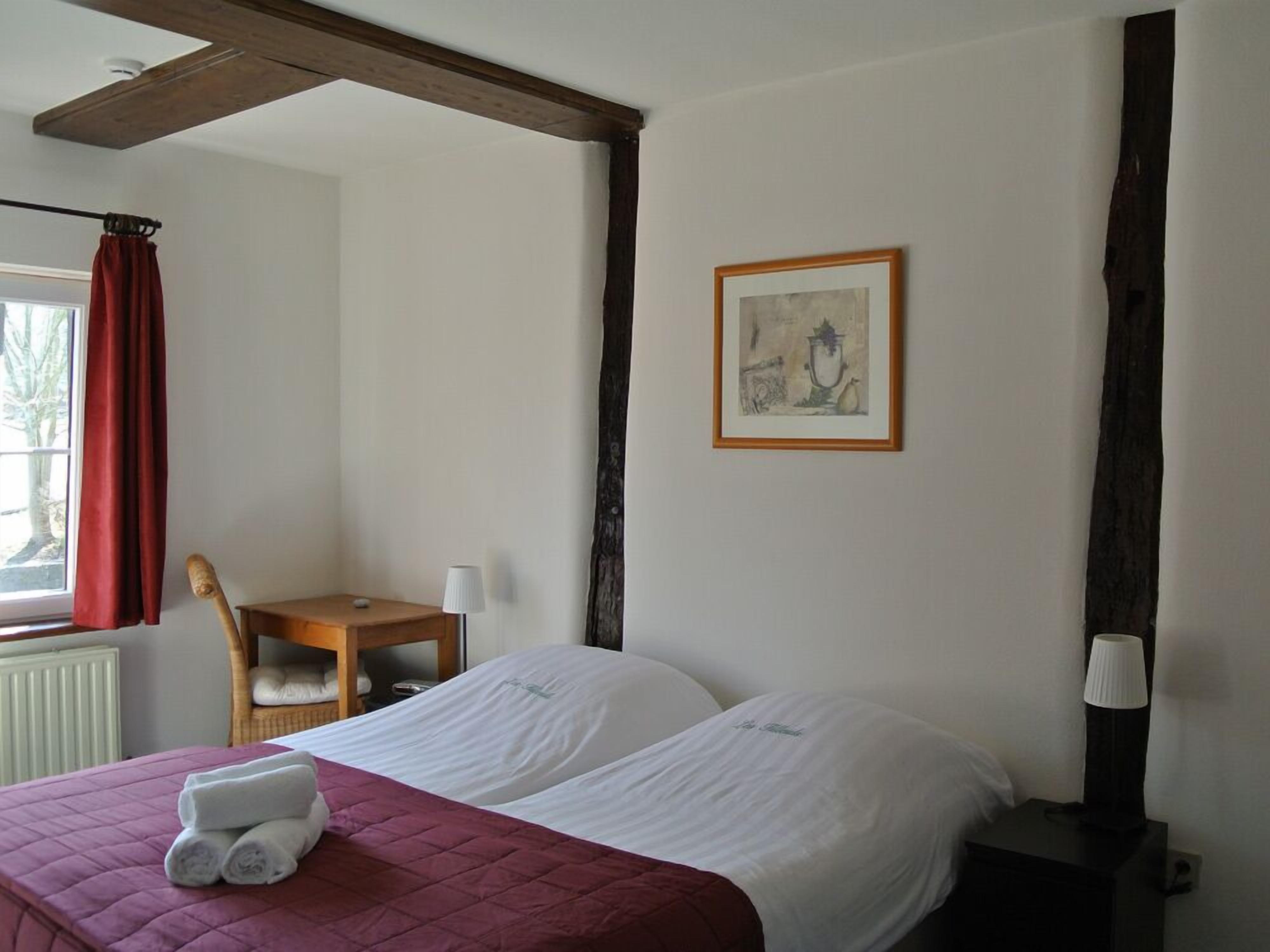 A hotel room with a bed, a desk, a chair, a lamp, and a framed picture on the wall.