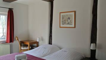 A hotel room with a bed, a desk, a chair, a lamp, and a framed picture on the wall.