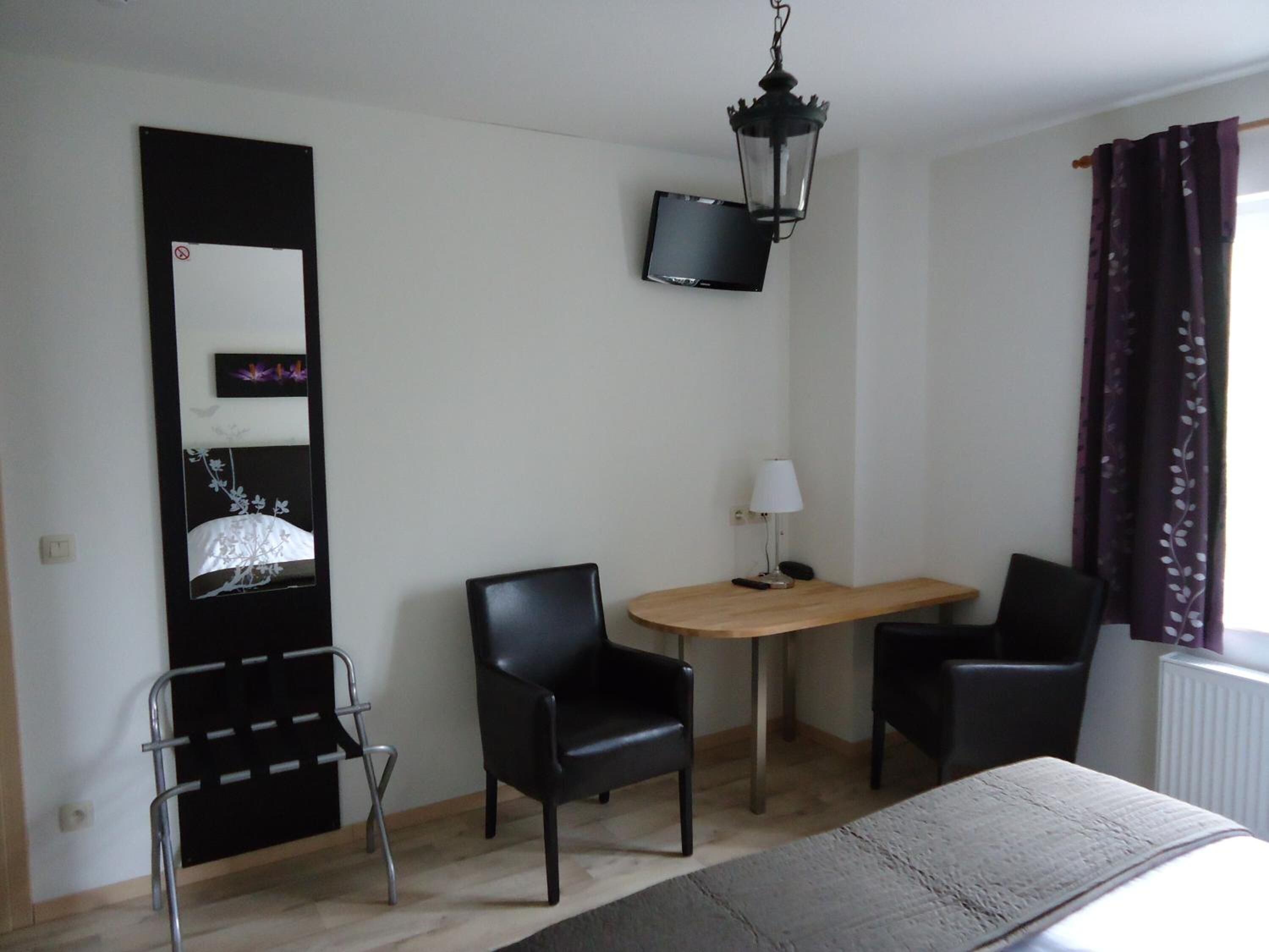 Una habitación de hotel con una cama, un escritorio con dos sillas, un televisor montado en la pared y una ventana con cortinas.