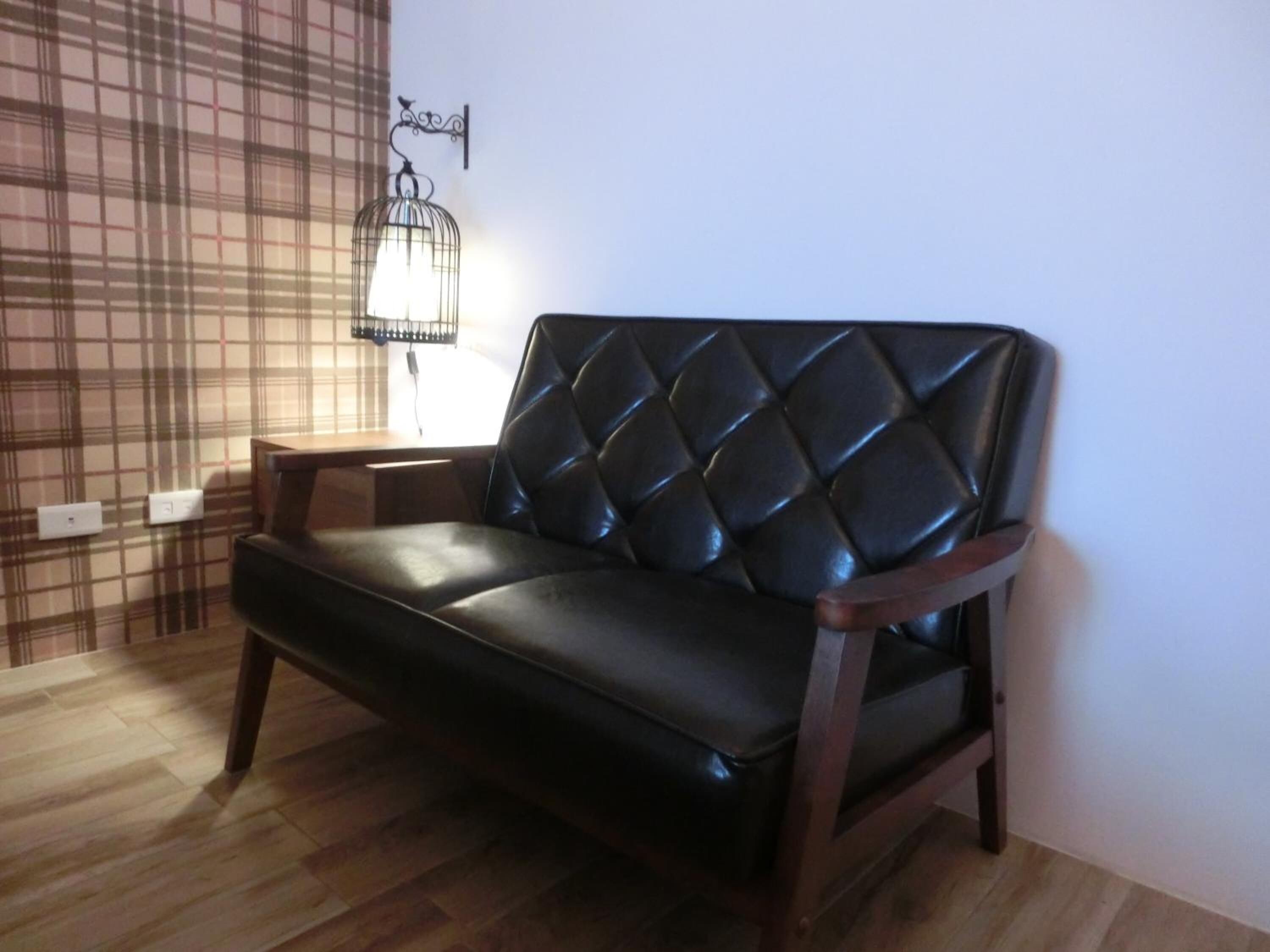 A black leather sofa with a diamond-patterned backrest in a room with wooden flooring and a plaid-patterned wall.