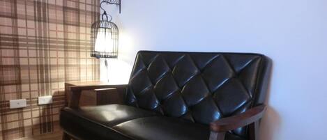 A black leather sofa with a diamond-patterned backrest in a room with wooden flooring and a plaid-patterned wall.
