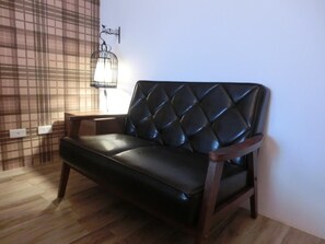 A black leather sofa with a diamond-patterned backrest in a room with wooden flooring and a plaid-patterned wall. - Chi Ya B&B (Hualien City)