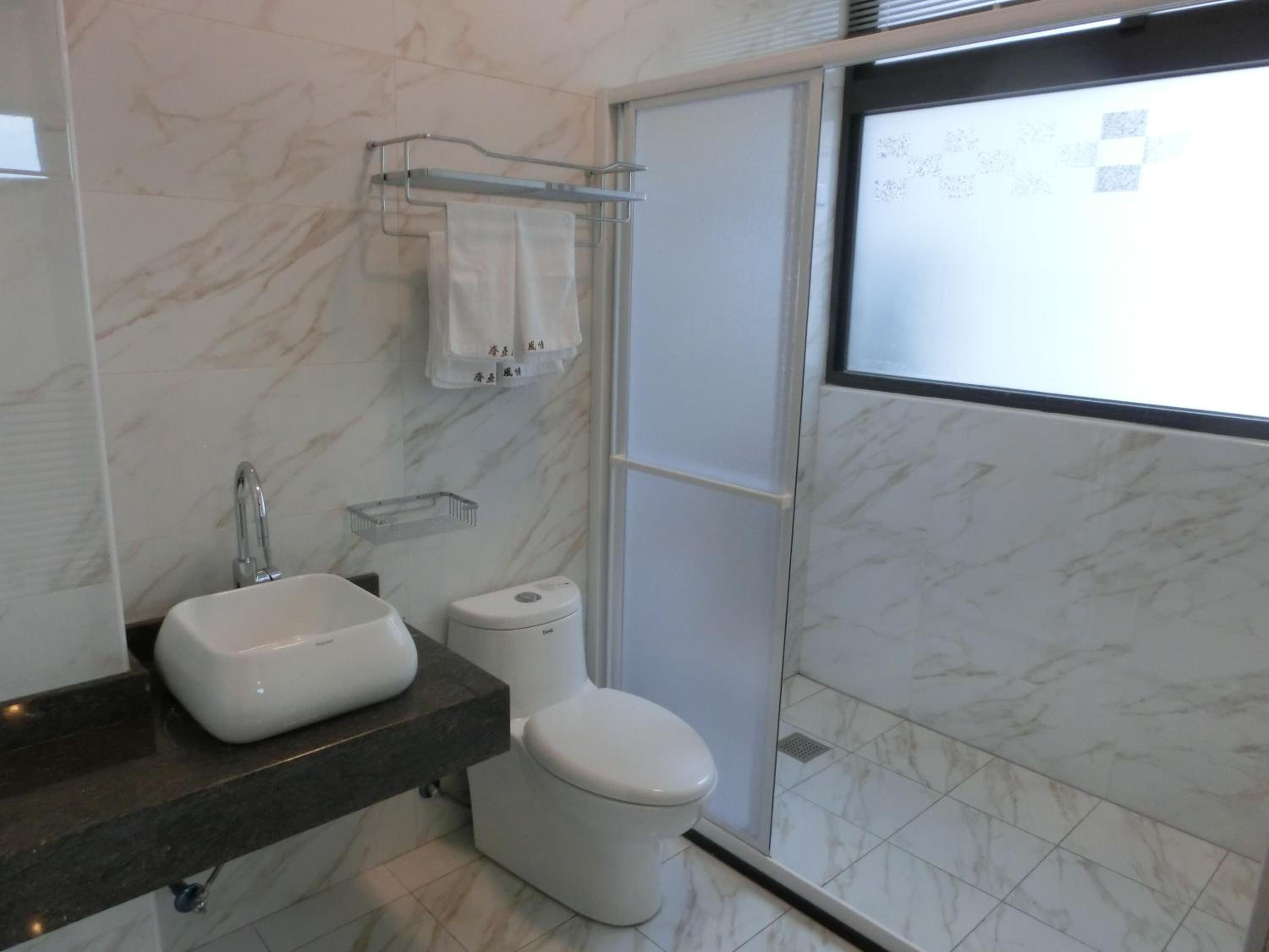 Et moderne badeværelse med marmorgulv, hvid vask, toilet og brusekabine i glas.