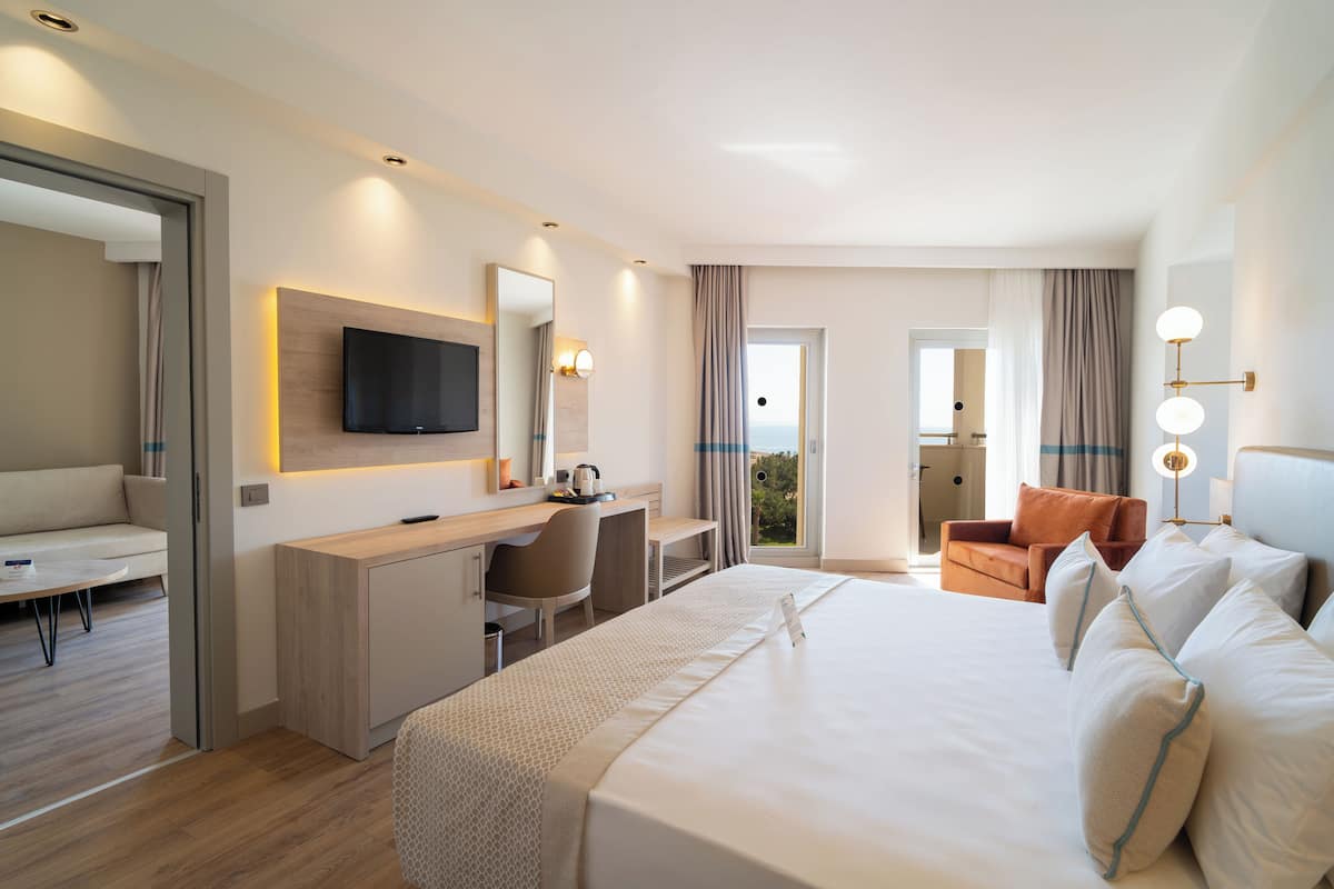 Quarto de hotel moderno com uma cama grande, uma escrivaninha, uma televisão e uma varanda com cortinas.