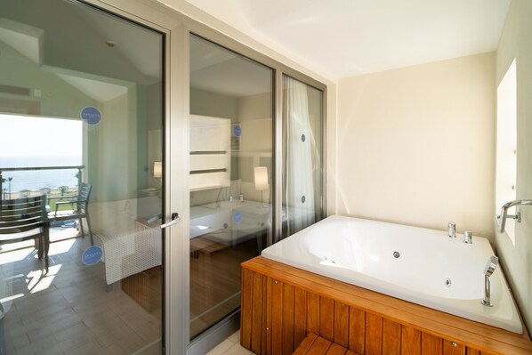 A modern bathroom with a large bathtub, a glass shower enclosure, and a view of the sea.