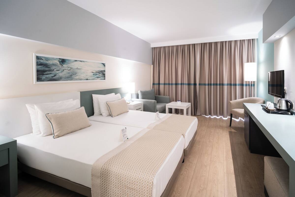 Quarto de hotel moderno com uma cama grande, uma escrivaninha, uma cadeira e uma televisão.