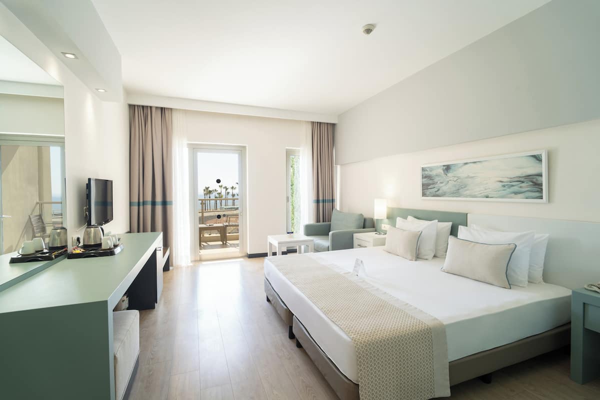 Quarto de hotel moderno com uma cama grande, uma escrivaninha com televisão de tela plana, uma mesinha e vista para o exterior.