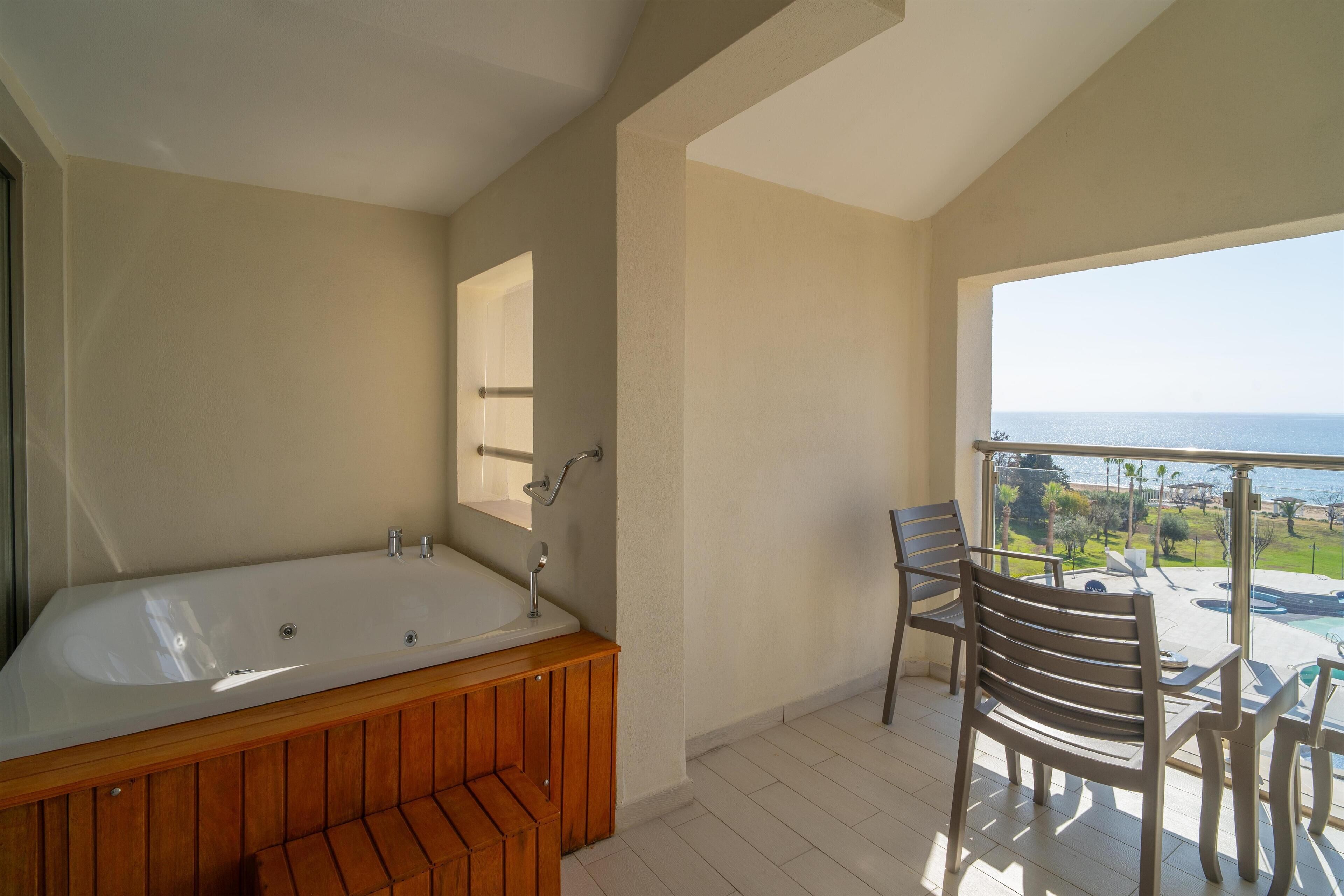 Un baño moderno con una bañera independiente, tocador de madera y un balcón con vistas al mar.