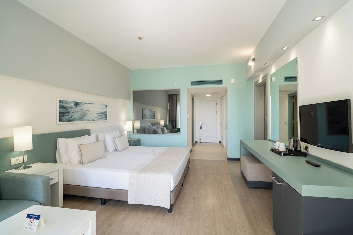 Quarto de hotel moderno com uma cama grande, mesas de cabeceira, televisão e banheiro visível através de uma porta aberta.