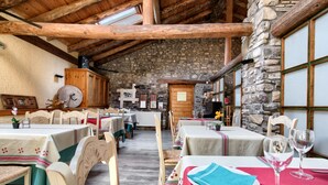 A rustic dining area with wooden tables and stone walls, featuring a stone fireplace and wooden beams. - Hostal Almadiero (Burgui)