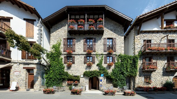 A stone building with multiple balconies, each adorned with red flowers. - Hostal Almadiero (Burgui)