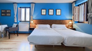 A room with two beds, a small table with a chair, and a window with curtains. - Hostal Almadiero (Burgui)