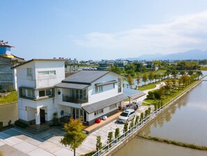 A modern two-story house with a balcony, a driveway, and a river in the background.
