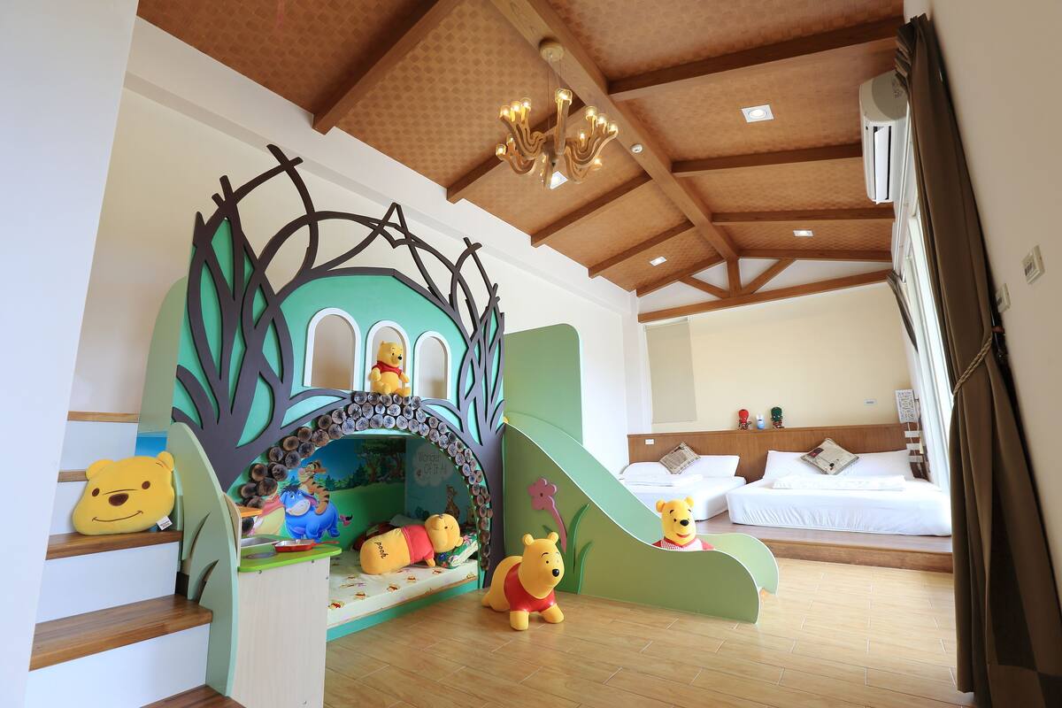 A children's play area with a slide, a bed, and a room with wooden beams and a chandelier.